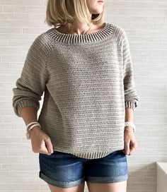 a woman standing in front of a brick wall with her hands on her hips wearing shorts and a sweater