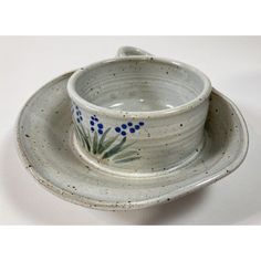 a white bowl with blue flowers on it and a saucer in the shape of a cup