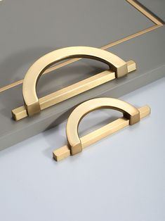 two brass handles on a gray surface with a gold frame in the middle and bottom