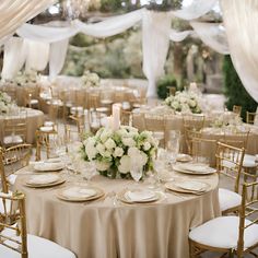 the tables are set with white flowers and gold chargers for an elegant wedding reception at the park