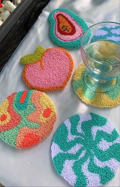 four colorful coasters on a table next to a glass of water and marshmallows