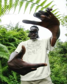 a man holding his hands up in front of some trees and bushes with one hand extended out