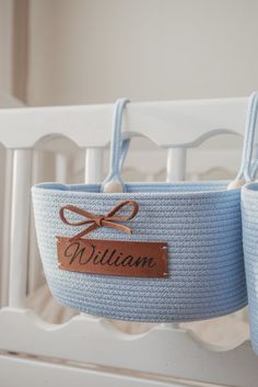 two baskets with name tags on them hanging from the side of a white crib