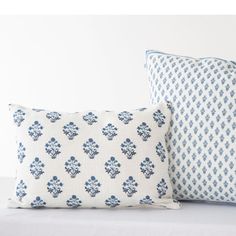 two blue and white pillows sitting on top of a bed next to each other in front of a white wall