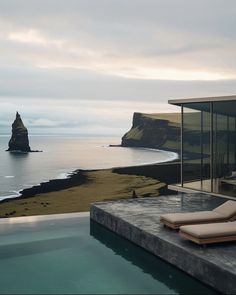 an outdoor swimming pool overlooking the ocean and rocky coastline with lounge chairs on it's edge