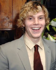 a young man in a suit and tie smiling at the camera with flowers behind him