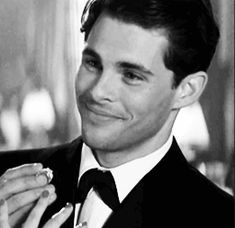 a man in a tuxedo is smiling and holding a ring on his finger
