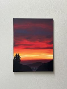 a painting hanging on the side of a wall with a sunset in the sky behind it