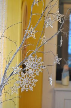 a branch with snowflakes hanging from it in front of a yellow door and window