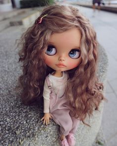 a close up of a doll with long hair sitting on a rock next to a sidewalk