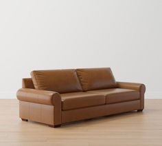 a brown leather couch sitting on top of a hard wood floor next to a white wall