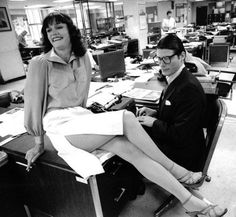 a woman sitting on top of a desk next to a man