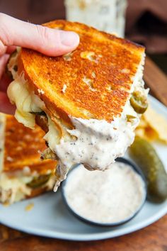 a person is holding up a grilled cheese sandwich with pickles and ranch dressing