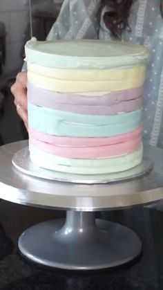 a woman holding a cake with pastel colors on it