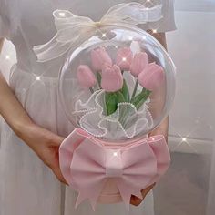 a person holding a vase with pink flowers in it and a bow on the side