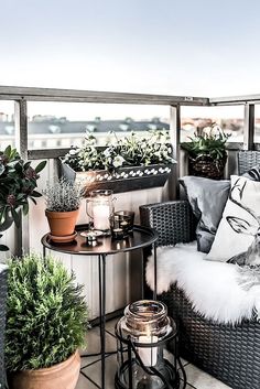 an outdoor balcony with potted plants and candles on the table, next to a wicker chair