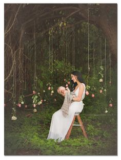 a woman sitting on a stool in front of a tree with flowers hanging from it