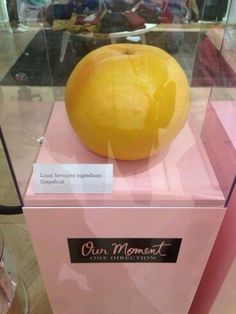 an orange sitting on top of a pink box in a glass case with writing underneath it