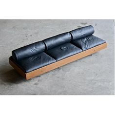 a black leather couch sitting on top of a cement floor next to a wooden frame