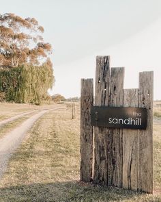 a wooden post with a sign that says sandhill on it in front of a dirt road