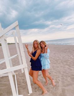 two beautiful young women standing on top of a sandy beach next to a white structure