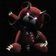 a red teddy bear with spikes on it's head and eyes, sitting in the dark