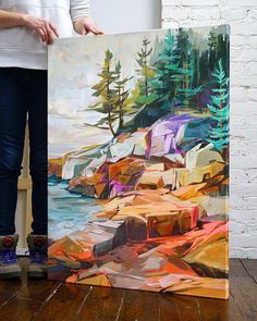 a person holding up a painting in front of a brick wall with trees on it