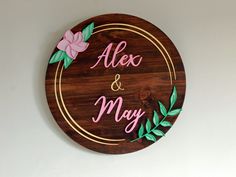 a wooden sign that says alex and may with flowers on the front in gold lettering