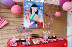 a red table topped with lots of desserts next to pink and purple balloons hanging from the ceiling