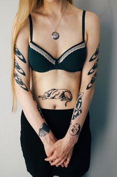 a woman with tattoos on her arms and chest standing in front of a white wall