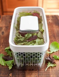 lettuce in a container sitting on top of a wooden table next to leaves