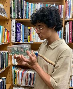 a man is looking through a plastic bag in front of a bookshelf full of books