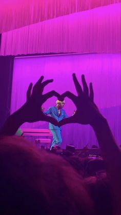 two hands making a heart shape in front of a stage with purple lights and curtains