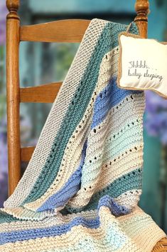 a crocheted blanket sitting on top of a wooden chair next to a pillow