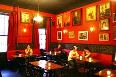 people sitting at tables in a restaurant with red walls and pictures hanging on the wall