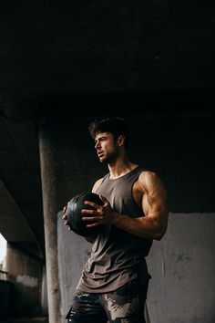 a man holding a ball in his right hand and looking at the camera while standing under an overpass