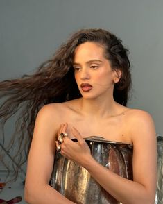 a woman with long hair standing in front of a metal bucket and holding her hands on her chest