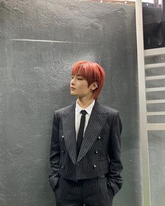 a man with red hair wearing a suit and tie standing in front of a wall