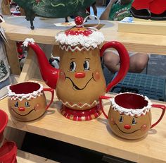 a tea pot and two mugs with faces painted on them sitting on a table