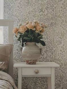 a vase filled with flowers sitting on top of a white table next to a bed