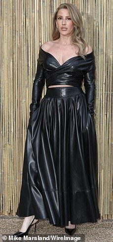 a woman in a black leather dress posing for the camera with her hands on her hips