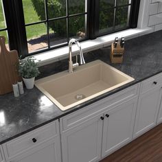 a kitchen sink sitting under a window next to a cutting board and potted plant