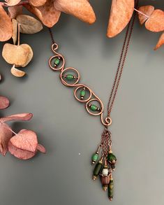 a necklace with green glass beads hanging from it's side on a table next to leaves