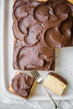 a piece of cake with chocolate frosting on a plate next to a knife and fork