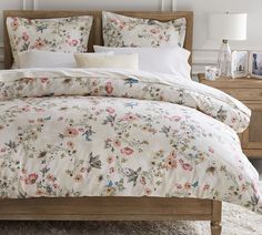 a bed with floral comforter and pillows on it in a bedroom next to two lamps