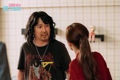 a man with long hair standing next to a woman in a red shirt and black t - shirt