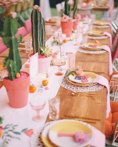 a long table with plates and place settings on it, along with cactus plants in pots