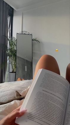 a person laying in bed reading a book with their feet up on the bed and one hand holding an open book