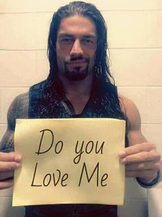 a man with long hair holding a sign that says do you love me on it