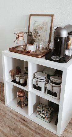 a white shelf filled with dishes and cups on top of a hard wood floor next to a wall